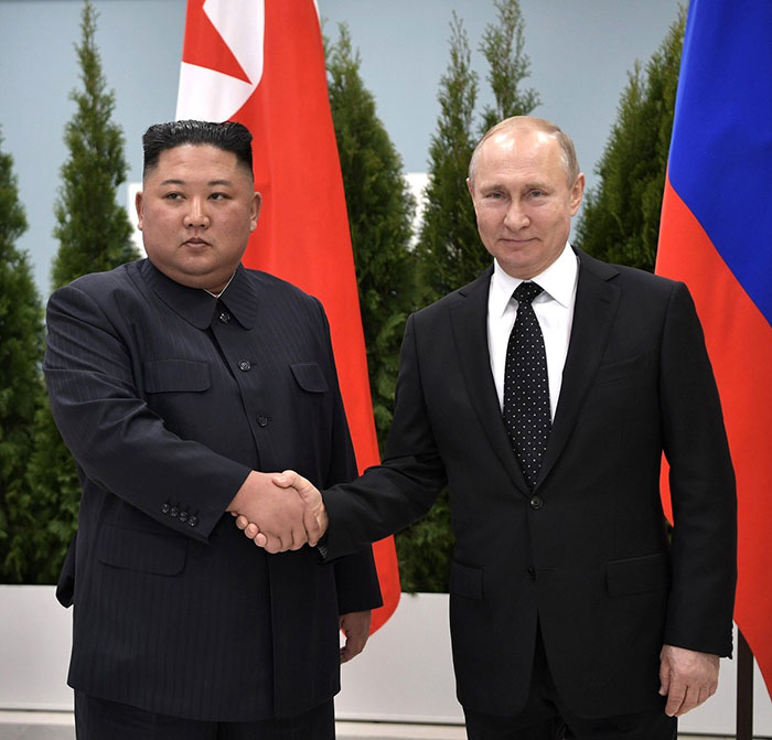 Two leaders shake hands with flags in the background, discussing North Korean troop deployment in Ukraine conflict.