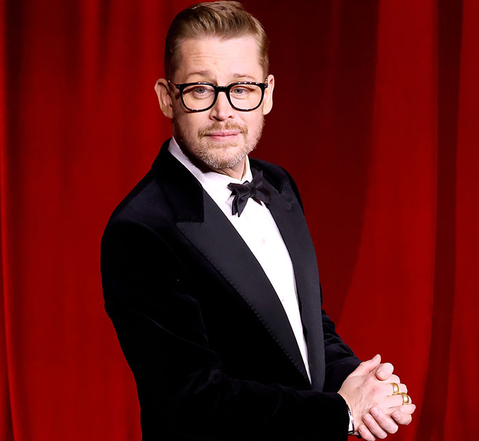 Man in a tuxedo posing on a red background at an event.