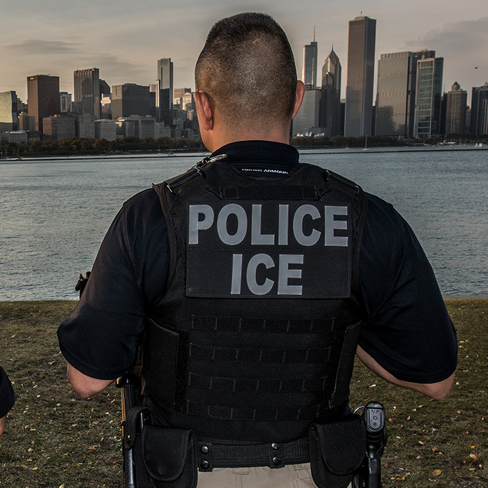 ICE police officer standing near water with city skyline in the background, related to U.S. citizen children deportation issue