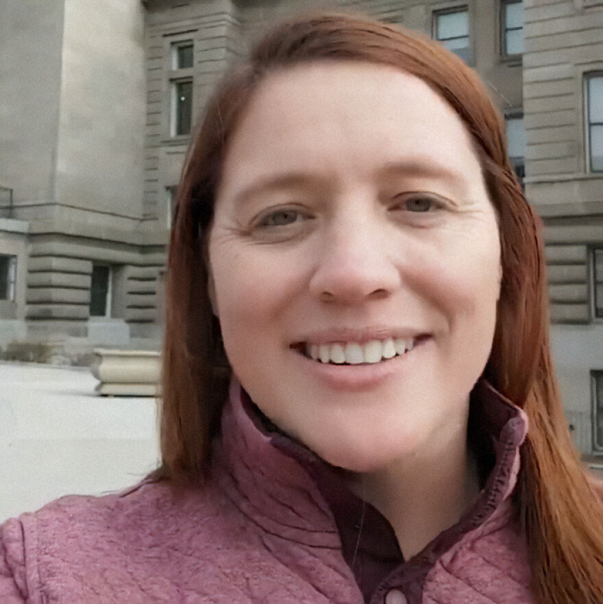A woman in a maroon jacket smiling outdoors with a building in the background. Republican town hall incident context.