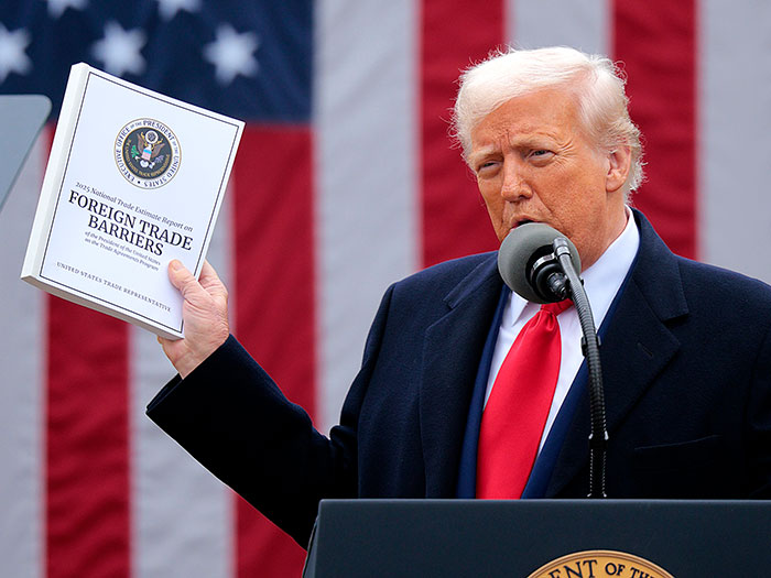 Person at podium holding a document on foreign trade barriers against an American flag backdrop, related to MAGA and Republicans.