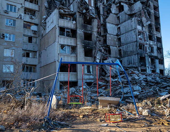 Damaged building and swing set amid Ukraine conflict, highlighting North Korean troop deployment acknowledgment.