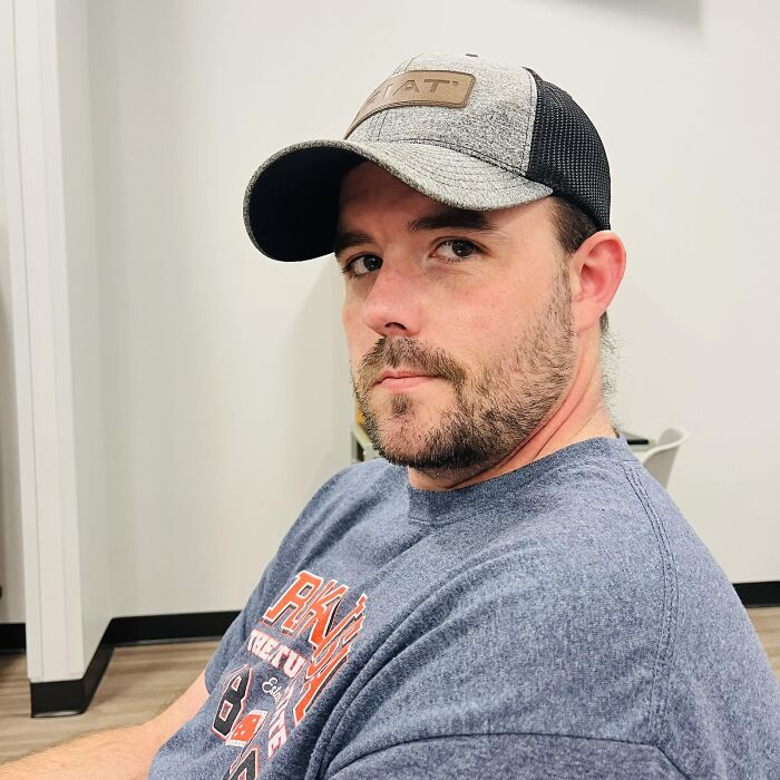 Man wearing a gray and black cap and blue shirt, sitting indoors, related to couple allegedly forcing girl survival on one Pop-Tart.