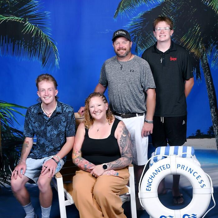 Family of four posing in tropical setting with palm trees, beach backdrop, and life preserver labeled Enchanted Princess.