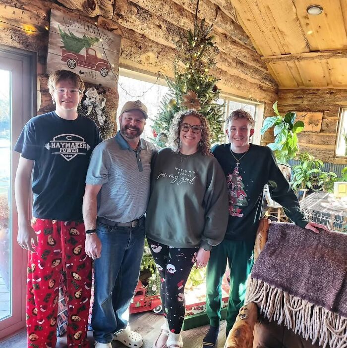 Family of four posing together indoors near a decorated Christmas tree in a cozy wooden cabin setting.