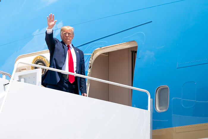 Former President Trump waving from airplane stairs, related to private prison pals and migrant crackdowns potential profits.
