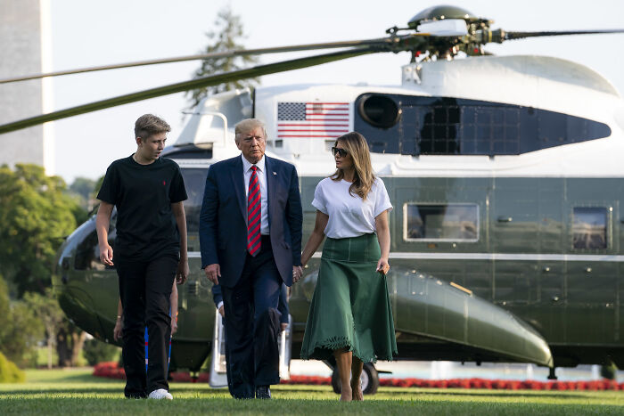 Melania Trump with Donald Trump and Barron walking on grass near helicopter amid rumors about Barron&rsquo;s college hunt.