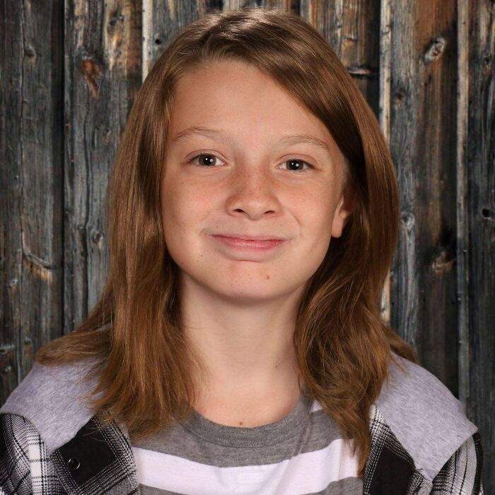 Portrait of a young boy, age 11, with medium-length brown hair and a slight smile, against a wooden background.