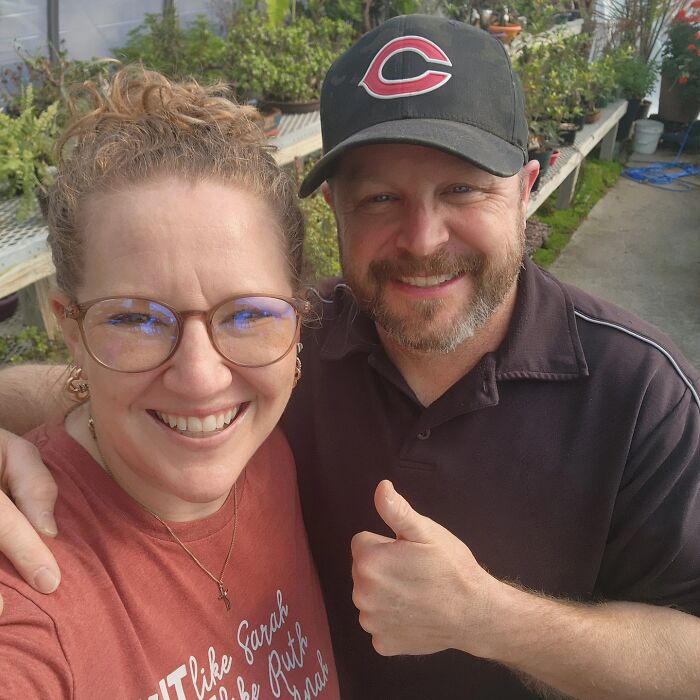 Smiling couple posing for a selfie outdoors surrounded by plants, related to family of four suspected murder-suicide case.