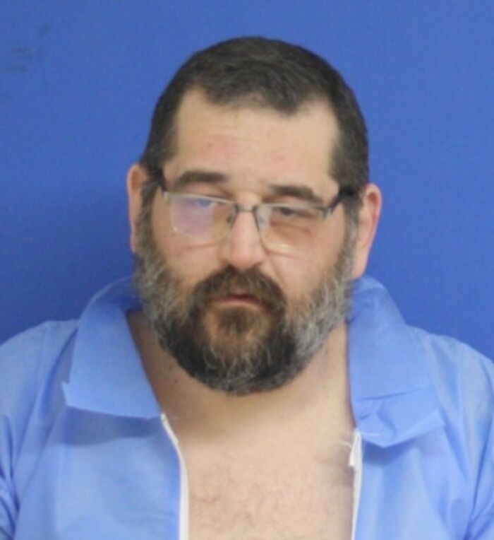 Man allegedly involved in fatal beating of 12-year-old son with baseball bat, wearing glasses and blue shirt.