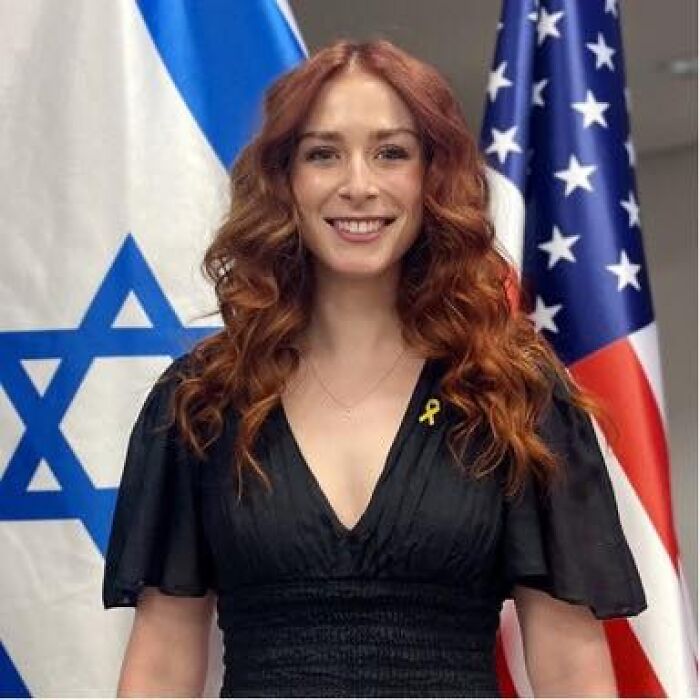 Woman with red hair standing between Israeli and American flags, related to Israeli Embassy couple fatally shot incident.