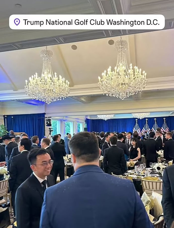 Crowd of crypto bros in formal attire mingling at Trump National Golf Club event with chandeliers and American flags in background.