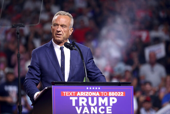 Speaker at podium during a crowded event, related to Health Secretary RFK Jr. swimming with grandkids in sewage-filled creek.