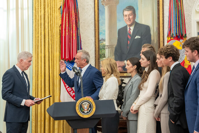 Man being sworn in with family by official at presidential event, related to Trump choosing wellness influencer surgeon general.