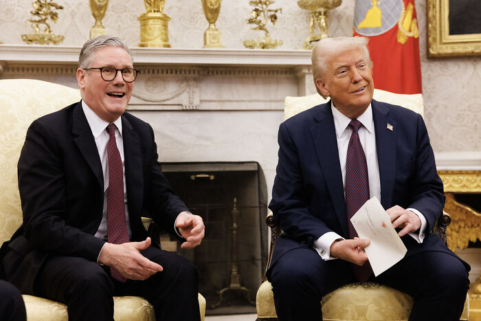 Two men in suits seated in a formal room, highlighting Trump&rsquo;s tariff strategy while China quietly wins global trade.