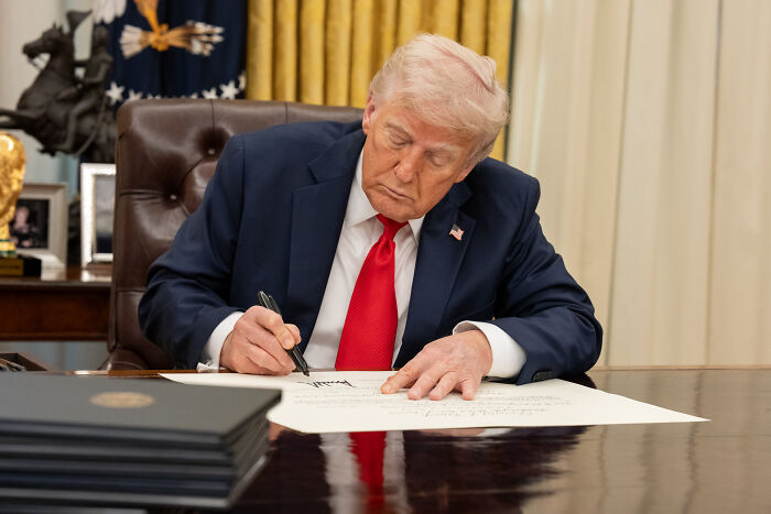 Former President Trump in the Oval Office signing documents amid tariffs while China advances in global trade.