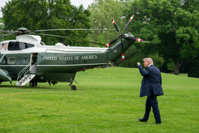 Donald Trump walking on grass near United States helicopter, related to reopening and expanding Alcatraz prison plans.