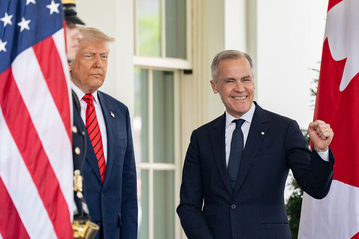 Donald Trump and a Canadian official standing near U.S. and Canadian flags discussing bold defense deal and Canada as 51st state.