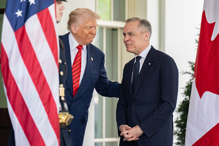 Donald Trump in a suit with red tie speaking to an ally with American and Canadian flags, representing global trade tensions and tariffs.