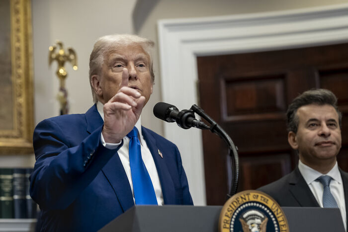 Former President Trump speaking at a podium with presidential seal, addressing government waste and policy issues.