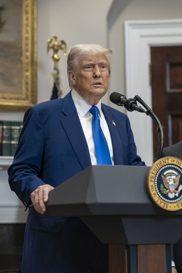 Donald Trump speaking at a podium during a public address about his overweight and neurotic pal&rsquo;s fat shot abroad.
