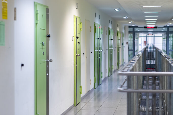 A long hallway in a detention center with green cell doors symbolizing child exploiters and offenders facing forced castration.