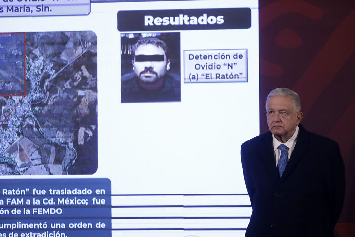 Man standing next to a screen displaying Mexican cartel family members and security information during a press event.
