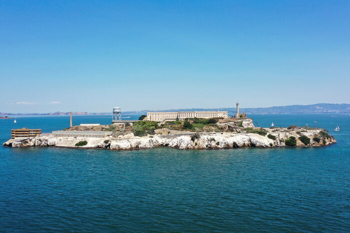 Aerial view of Alcatraz Island prison surrounded by water under clear blue sky, symbolizing Trump reopening and expanding prison.