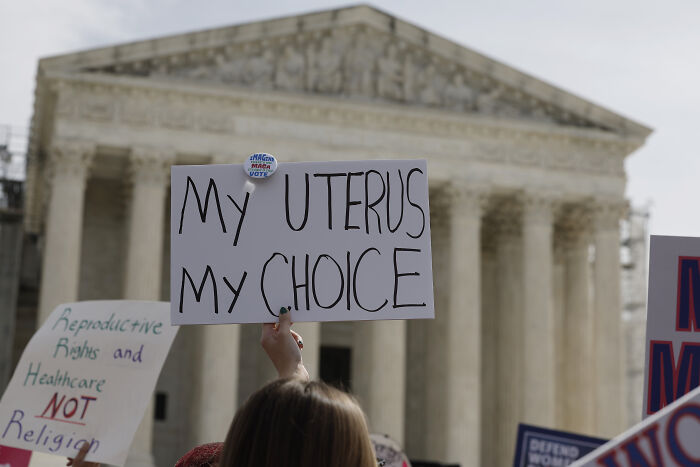 Protesters holding signs about reproductive rights outside a courthouse amid Michigan abortion law debate.