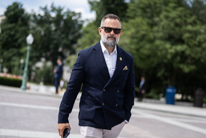 Man wearing sunglasses and navy blazer walking outdoors, related to Republican accused of lying about military service.