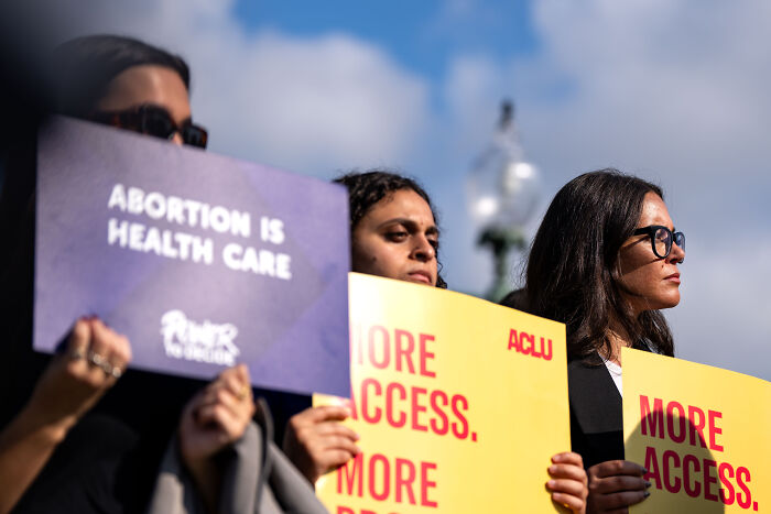 Protesters in Texas hold signs advocating abortion access amid police dystopian surveillance methods tracking women.