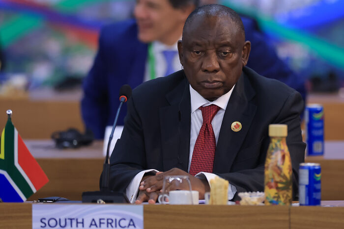 South African official at a conference table with a South Africa flag, representing white South Africans granted refugee status.