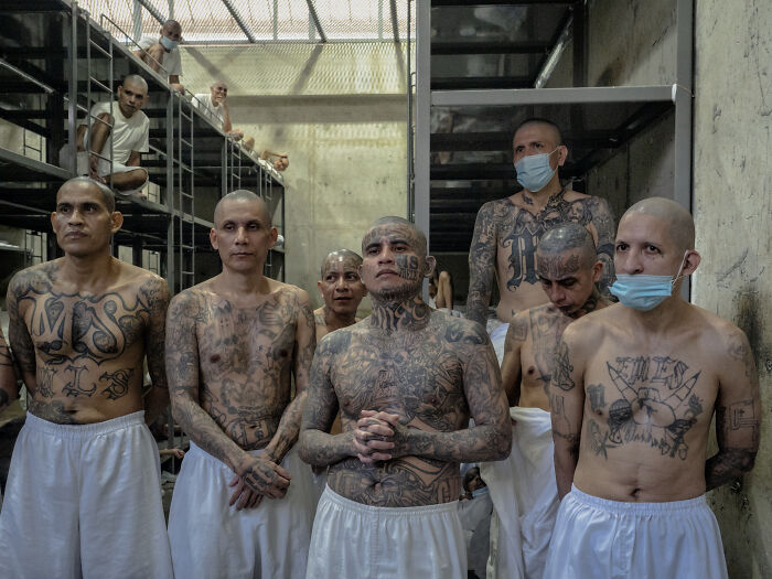 Group of tattooed migrants in detention facility, highlighting the urgent need for help in Texas through drone footage messages.