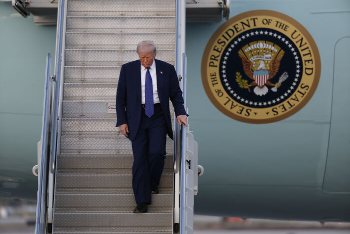 Donald Trump descending Air Force One stairs with presidential seal visible on the plane in an outdoor setting