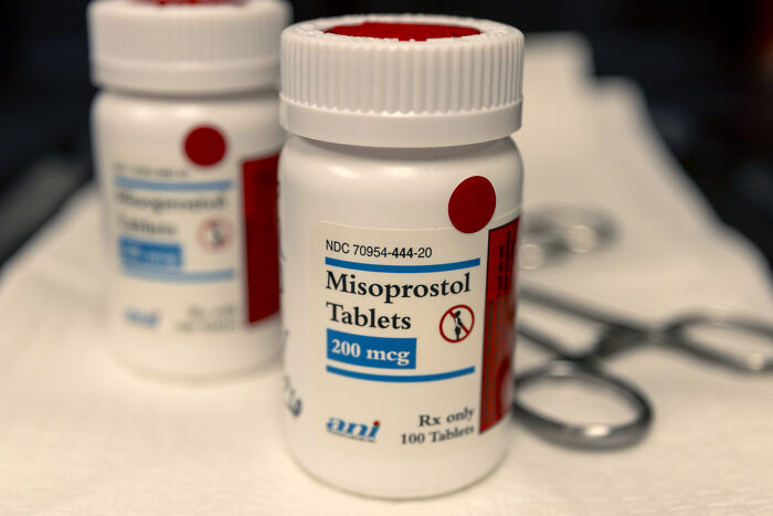 Bottle of Misoprostol tablets in focus with medical tools blurred in the background related to Michigan abortion law changes.
