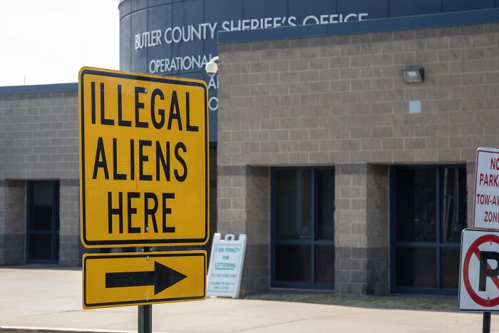 Yellow sign reading illegal aliens here with an arrow outside Butler County Sheriff&rsquo;s Office referencing Asian migrants deported to African country.
