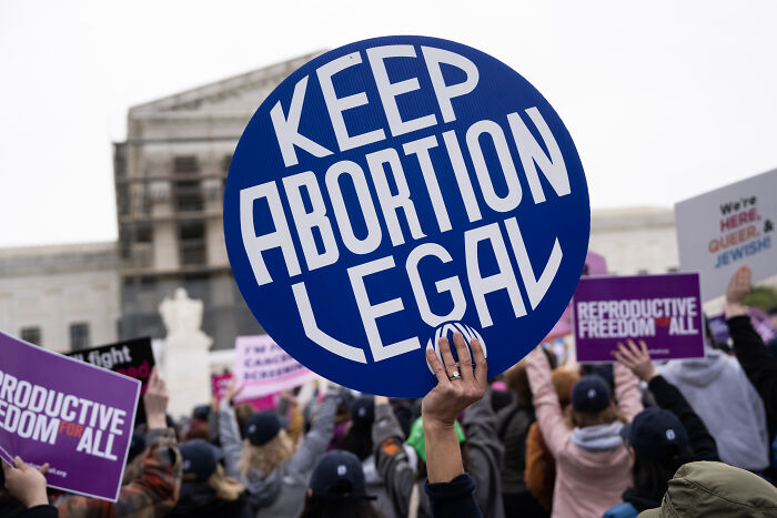 Crowd holding signs about abortion rights, with a focus on a blue sign saying keep abortion legal in a public protest.