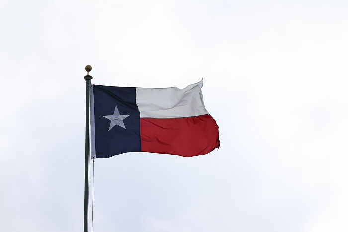 Texas flag waving on a pole representing police use of dystopian surveillance methods to track abortion care access.