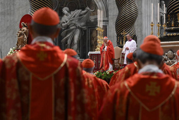 Catholic cardinals in red robes attending a religious ceremony inside a grand church in Rome.