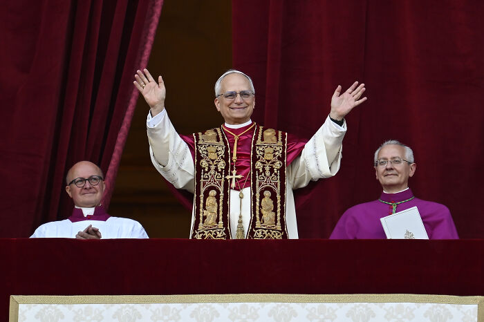 Pope Leo XIV in ceremonial robes with raised hands on balcony, sparking speculation about his agenda and MAGA reaction.