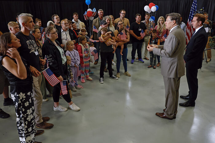 Group of people holding American flags listening to two men in suits, related to white genocide and South African president topics.