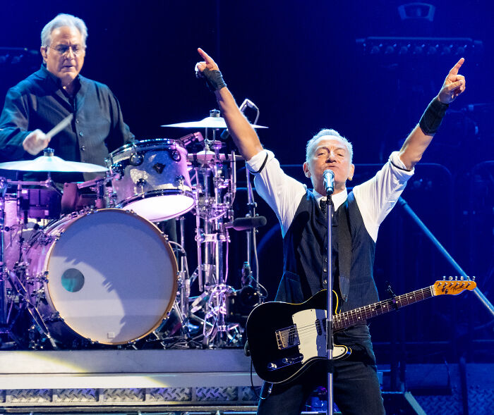 Bruce Springsteen performing live onstage with guitar and drummer, delivering a scathing message about Trump.