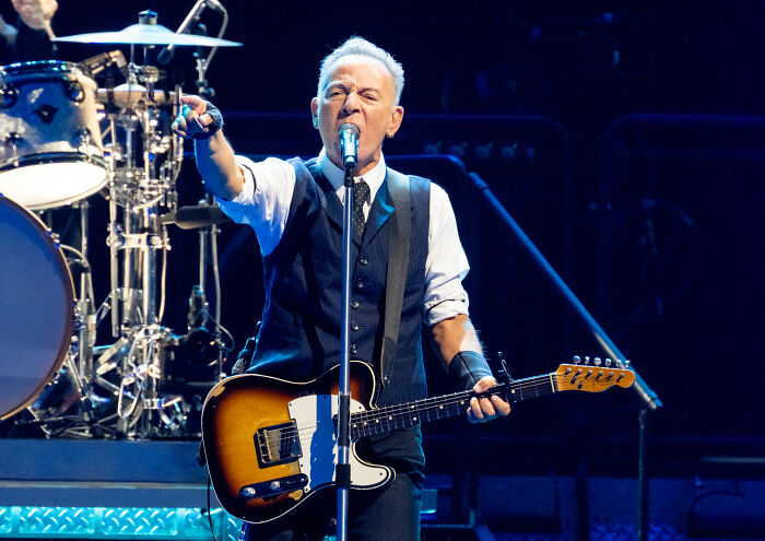 Bruce Springsteen performing live onstage passionately with guitar, delivering a scathing message about Trump.