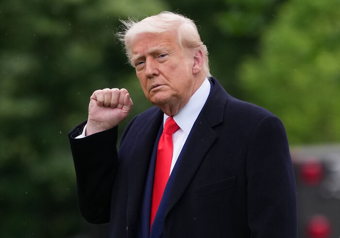 Former President Trump outdoors wearing a dark coat and red tie, raising his fist amid Larry Hoover sentence commutation news.