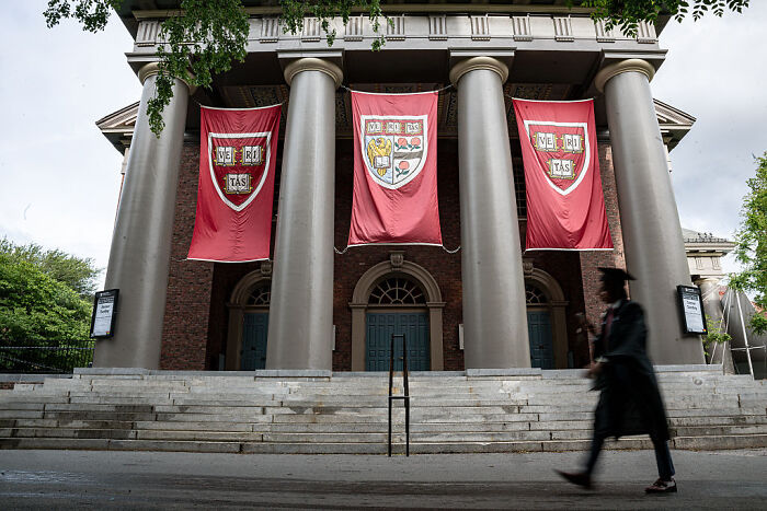 Harvard University building with banners and a person in graduation attire walking by, related to Barron&rsquo;s college hunt.