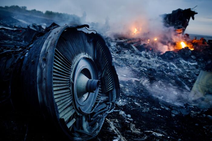 Wreckage of MH17 crash site with smoldering fires, focused on damaged aircraft engine after downing incident.