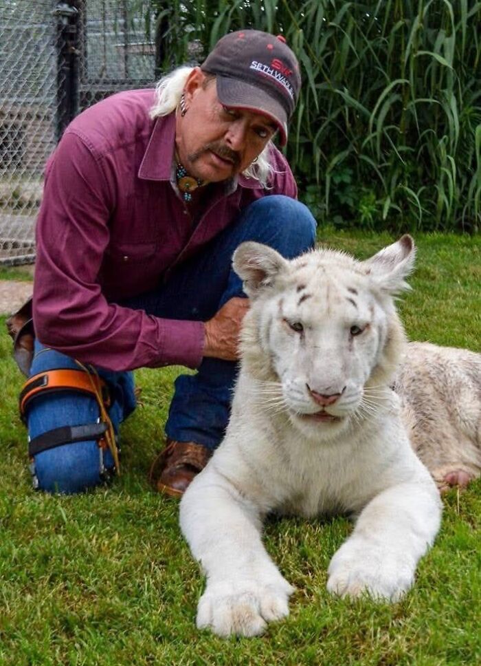 Man kneeling on grass with a white tiger cub, relating to Trump deporting Joe Exotic&rsquo;s husband.