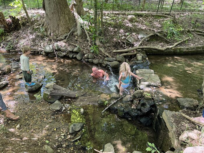 Health Secretary RFK Jr. swimming with grandkids in a creek contaminated with sewage and bacteria in a forest setting.
