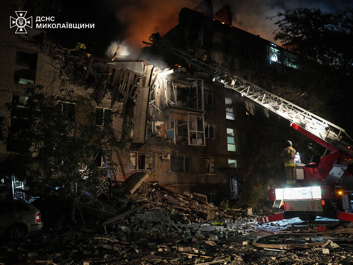 Firefighters responding to damage from largest Russian attack on Ukraine, with building debris visible at night.