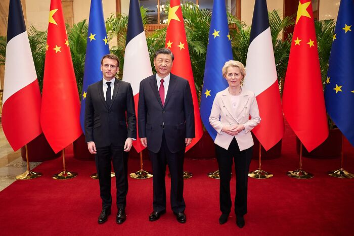 Leaders standing in front of China, France, and EU flags, highlighting China quietly winning the global trade game.